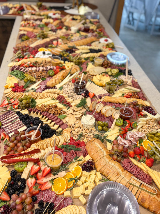 Extensive charcuterie board with various meats, cheeses, fruits, and vegetables on a long table.